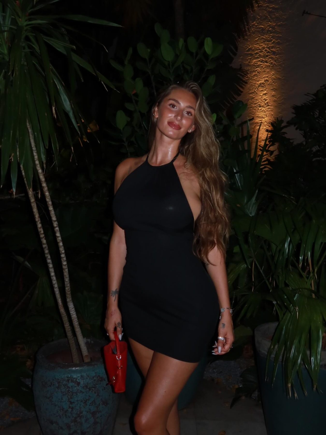 Ruby Reid in a black halter mini dress among tropical greenery at night in Miami